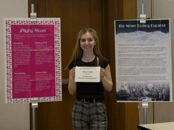 Claire Callen stands between two large posters displaying her projects.